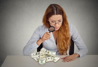 woman looking through magnifying glass on stack of dollar banknotes clipart