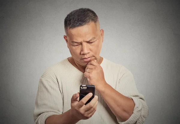 Homem segurando olhando para o seu telefone inteligente isolado fundo parede cinza — Fotografia de Stock