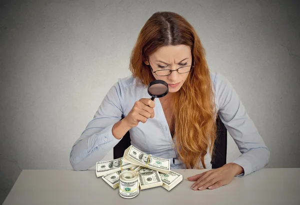 Woman looking through magnifying glass on stack of dollar banknotes — Stock Photo, Image