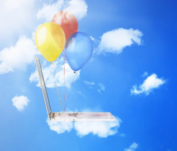 Ноутбук с красочными воздушными шарами, летящими высоко в голубом небе — стоковое фото