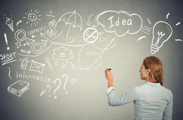 Mujer escribiendo con pluma muchas ideas en pizarra de pared gris — Foto de Stock