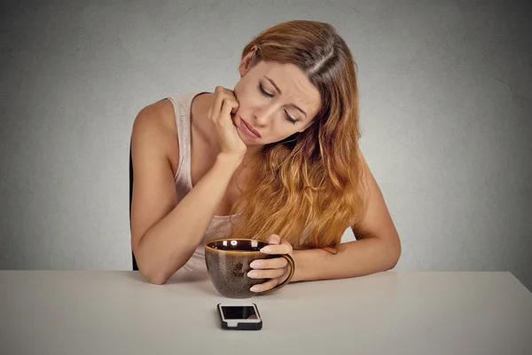 Mulher triste sentada à mesa olhando para o telefone móvel — Fotografia de Stock