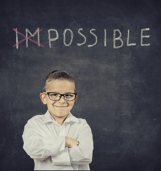 Smart smiling boy standing in front of blackboard — Stock Photo, Image