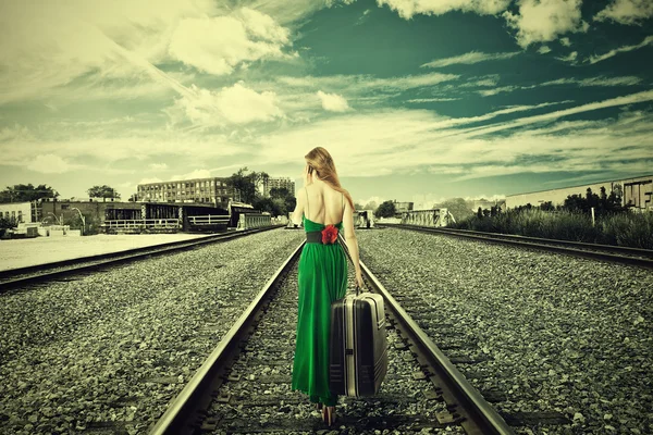 Νεαρή γυναίκα με βαλίτσα περπάτημα μακριά σε σιδηροτροχιές που μιλάει στο τηλέφωνο — Φωτογραφία Αρχείου
