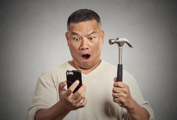 Shocked man looking at smart phone holding hammer — Stock Photo, Image