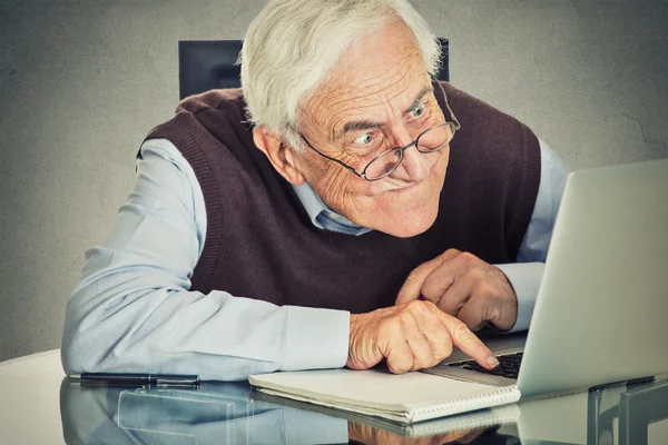 Idoso velho usando computador portátil sentado à mesa — Fotografia de Stock