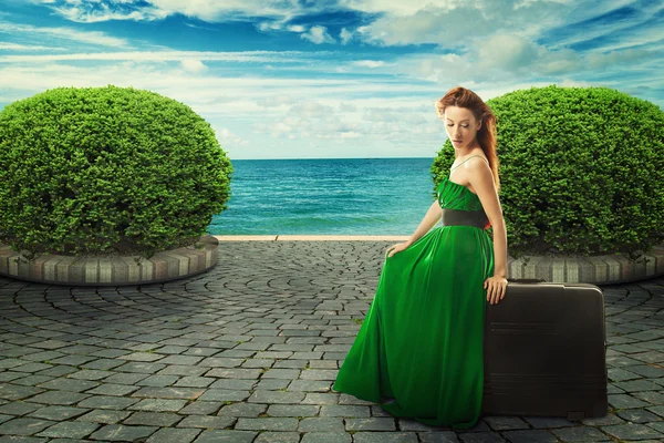 Beautiful woman in green dress sitting on a suitcase — Stock Photo, Image