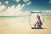 woman sitting in a glass jar on a beach looking at the ocean view