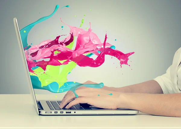 Hands on keyboard with colorful splashes out of monitor — Stock Photo, Image