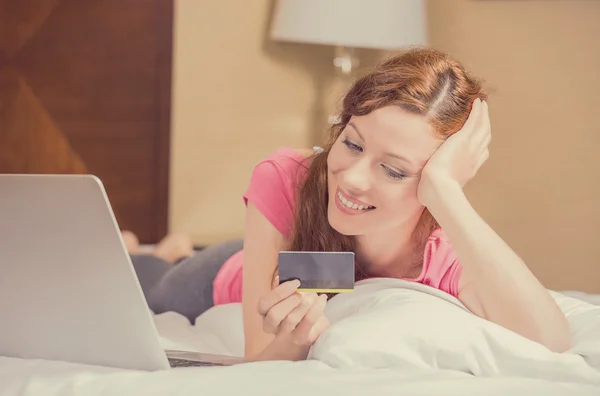 Γυναίκα, βάζοντας στο κρεβάτι με το lap-top κρατώντας πιστωτική κάρτα αγορών σε απευθείας σύνδεση — Φωτογραφία Αρχείου