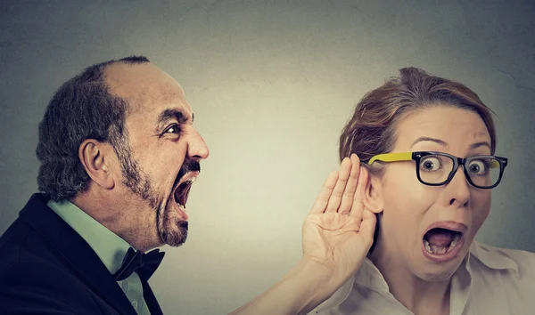 Angry man screaming curious woman with hand to ear gesture listens — Stock Photo, Image