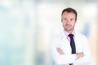 Kendine güvenen erkek doktor hastanede ayakta katlanmış silah gülümseyen 