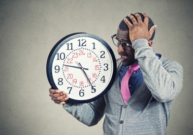 Stressed young man running out of time looking at wall clock  clipart