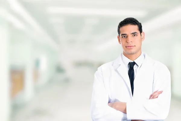 Médico masculino confiante sorrindo braços dobrados de pé no hospital — Fotografia de Stock