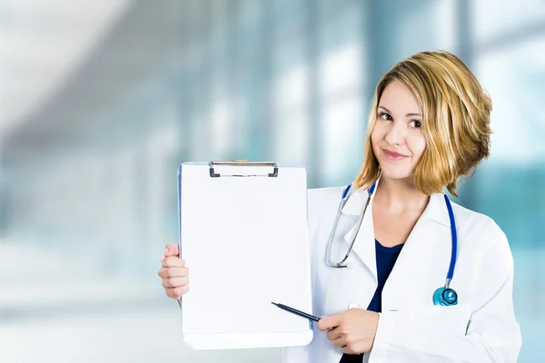 Happy smiling doctor with clipboard standing in hospital hallway — Stock Photo, Image