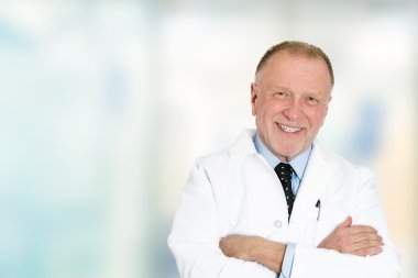 gülümseyen kıdemli doktor hastane koridorda kamera bakıyor 