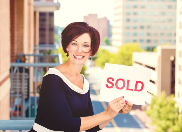 Real estate agent holding sold sign isolated on city background — Stock Photo, Image