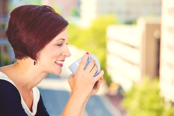 太陽の下で屋外に座ってコーヒーを飲む女性の笑みを浮かべてください。 — ストック写真