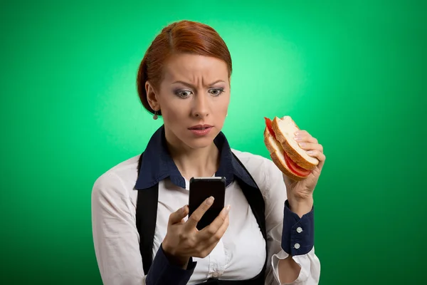 Donna d'affari guardando il telefono cellulare mangiare sandwich — Foto Stock