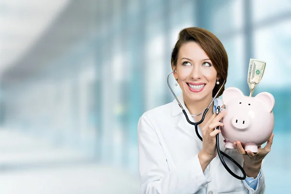 Médico sorrindo segurando ouvir banco porquinho com estetoscópio — Fotografia de Stock