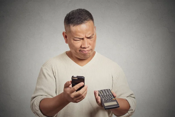 Homem confuso olhando para o seu telefone inteligente segurando calculadora — Fotografia de Stock