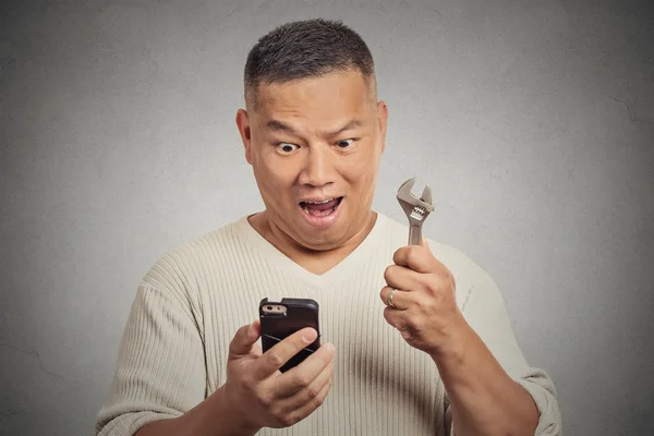 Hombre emocionado mirando el teléfono inteligente que sostiene el instrumento clave llave inglesa — Foto de Stock