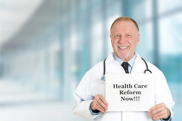 Doctor holding health care reform now sign standing in hospital — Stock Photo, Image