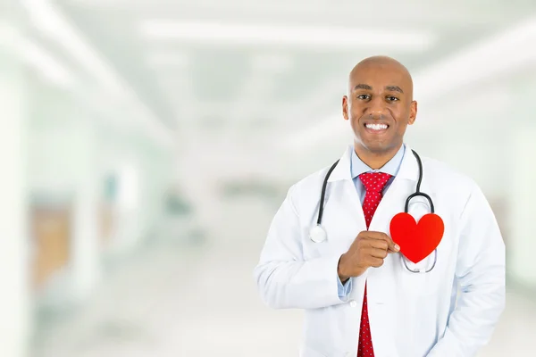 Feliz médico sosteniendo el corazón rojo de pie en el pasillo del hospital —  Fotos de Stock