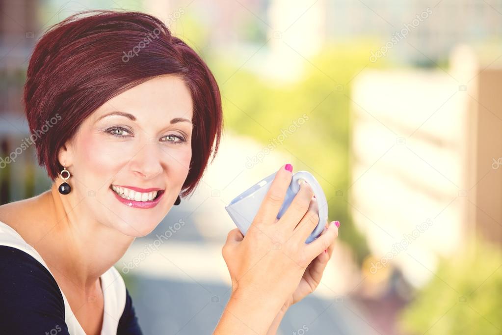 smiling woman drinking coffee in sun sitting outdoor