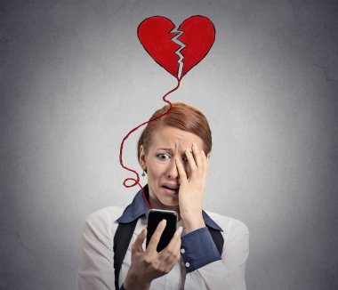 Sad woman with broken heart looking at her mobile phone clipart
