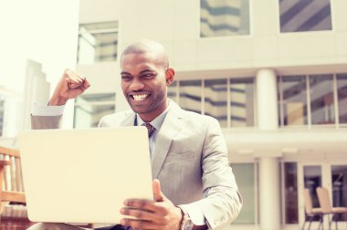 Happy successful young man with laptop computer celebrates success 