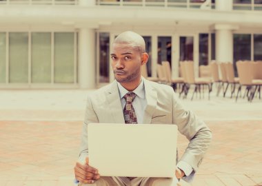 Business man with laptop skeptically looking at you camera