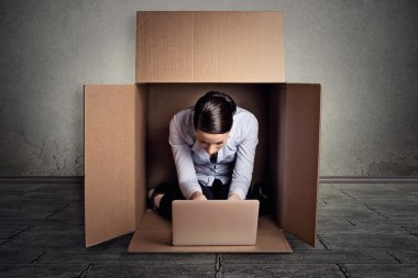 businesswoman sitting in carton box working on laptop computer 