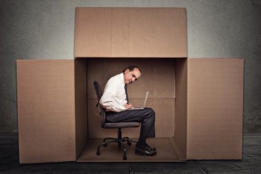 Man sitting in a box working on laptop computer 