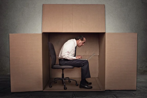 Человек, сидящий в коробке и работающий на ноутбуке — стоковое фото