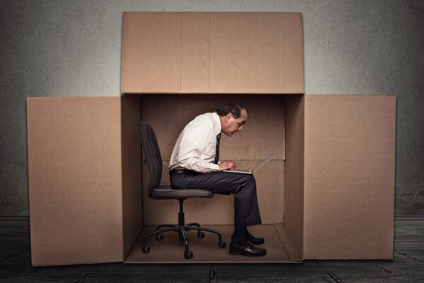 Man sitting in a box working on laptop computer 