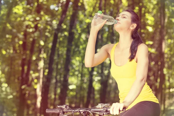 Ciclista jovem mulher em amarelo t-shirt ao ar livre beber água engarrafada — Fotografia de Stock