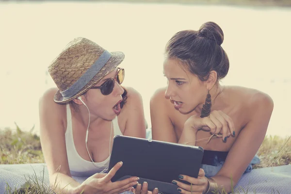 Dos chicas sorprendidas mirando pad discutir las últimas noticias de chismes — Foto de Stock