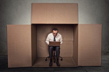 man working on laptop sitting on chair inside carton box clipart