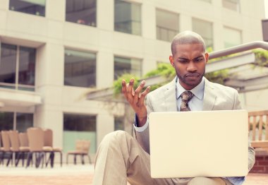 man sitting outside office looking at laptop frustrated about computer crash