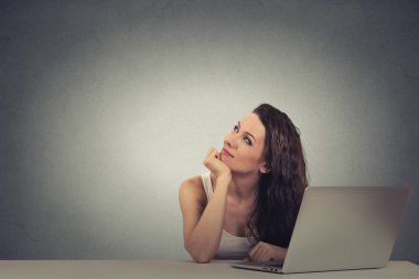 Thoughtful woman working on a laptop thinking looking up
