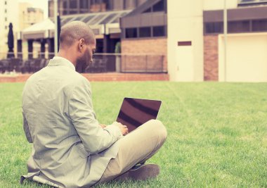 man sitting outside corporate office working on laptop computer 