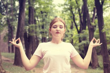 young woman meditating with eyes closed outdoors in park