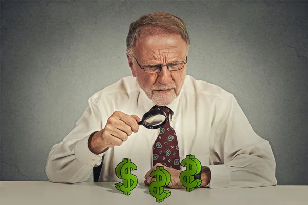 Skeptical business man looking through magnifying glass at dollar sign symbol — Stock Photo, Image