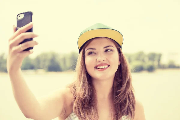 Frumoasă femeie tânără într-o capac luând selfie cu un smartphone — Fotografie, imagine de stoc