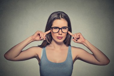 angry unhappy woman with glasses plugging ears with fingers