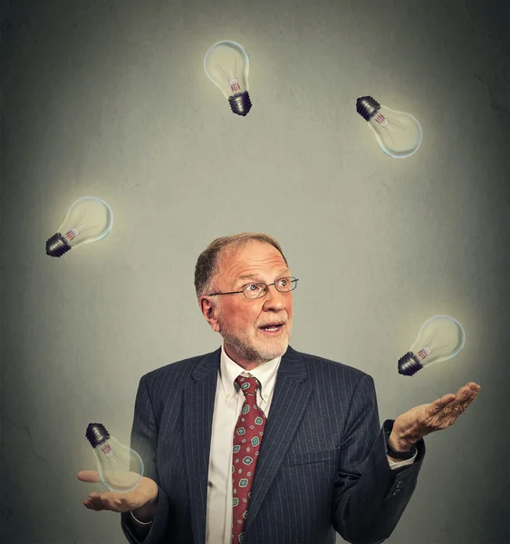 Ejecutivo senior hombre de negocios en traje malabares jugando con bombillas —  Fotos de Stock