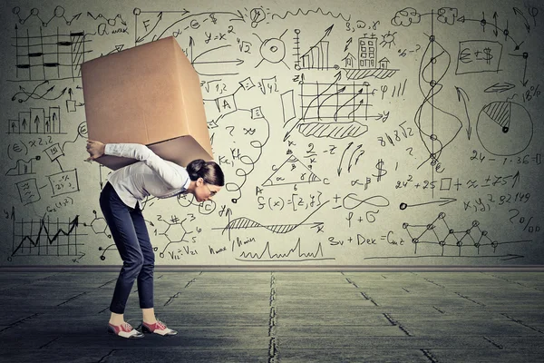 Woman carrying heavy box walking along gray wall — ストック写真