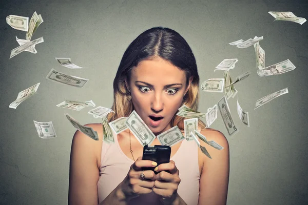 Shocked woman using smartphone dollar bills flying away from screen — Stockfoto