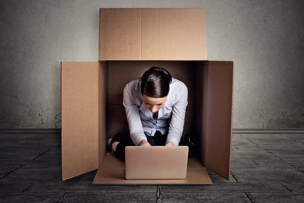 businesswoman sitting in carton box working on laptop computer 